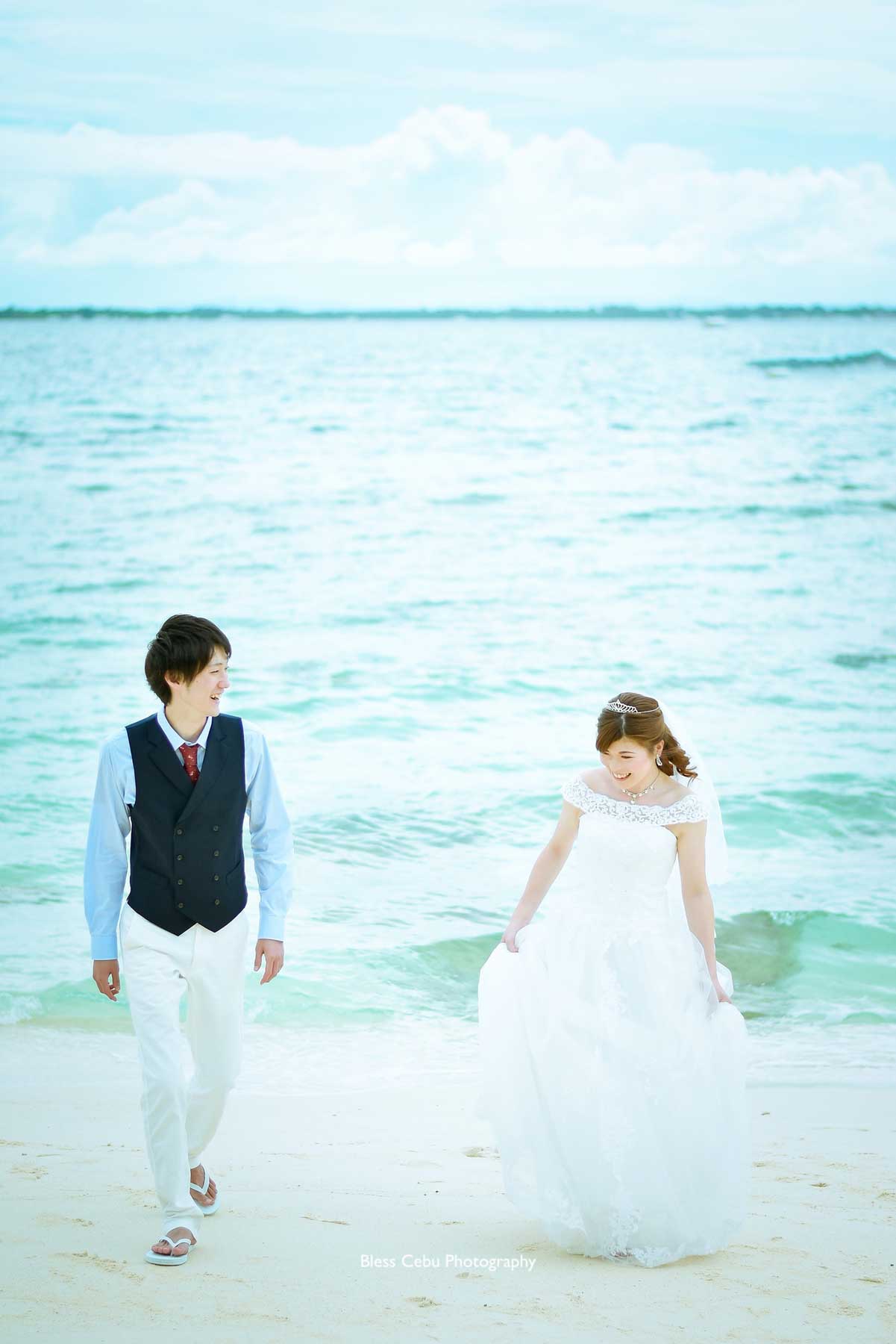 ドレスの裾を持って浜辺を歩く花嫁様