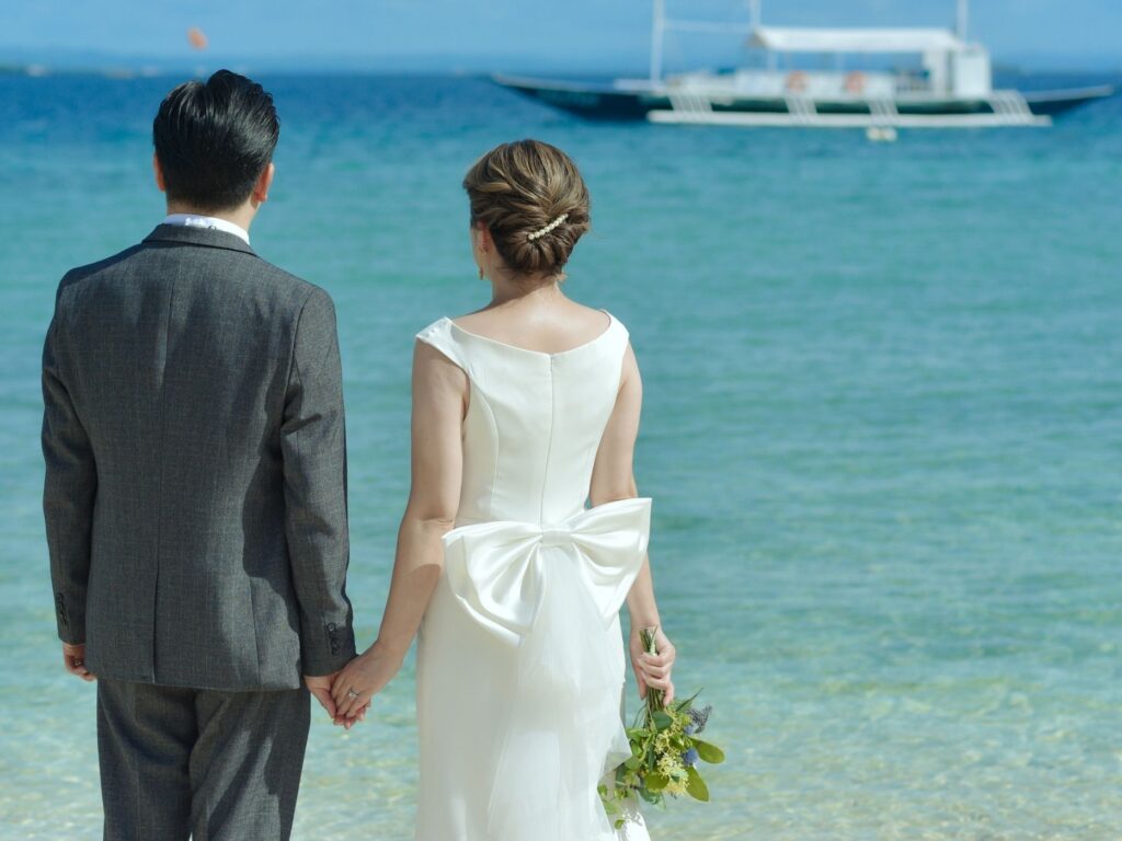 海を見つめながら手を繋ぐ新郎新婦の後ろ姿の前撮り写真